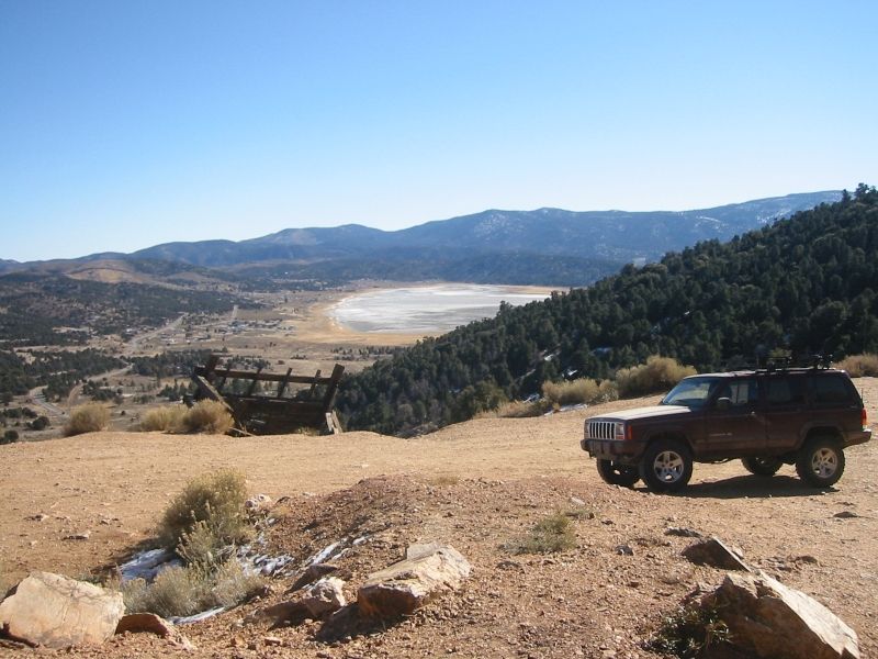 Maroon Jeep Cherokee XJ parked on a dirt overlook above a dry lakebed and mountains