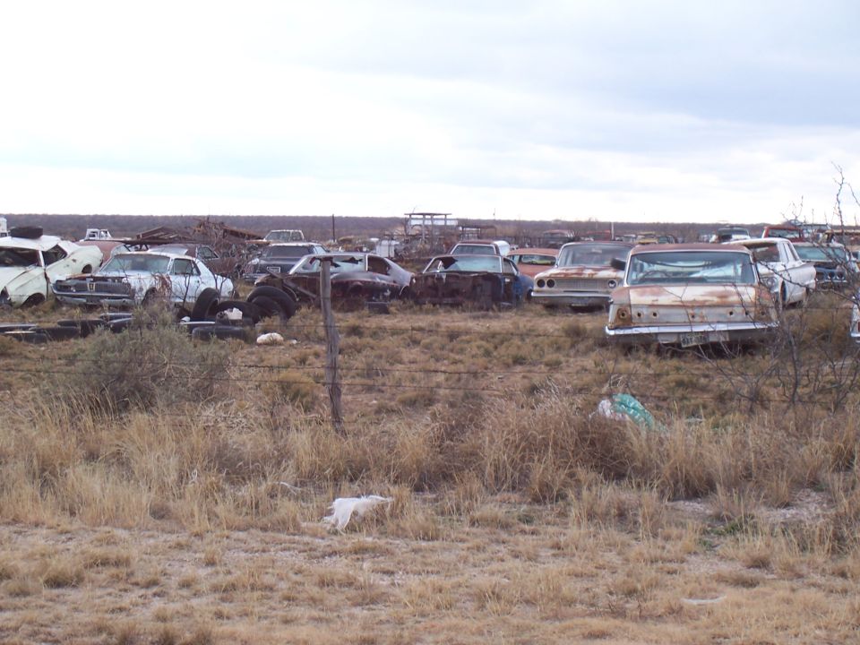 Junkyard scene with many rusted, dilapidated cars under a cloudy sky