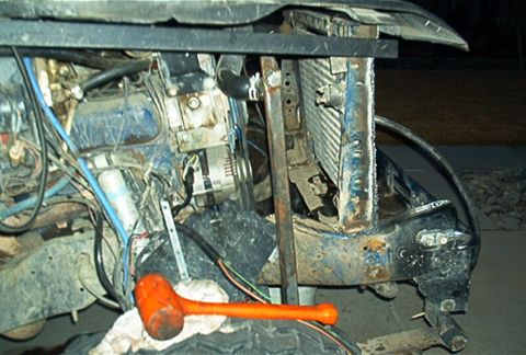 1986 Ford Bronco - Close-up view of a vehicle's engine bay, showing the radiator, alternator, and various hoses and wires, with an orange mallet in the foregr…