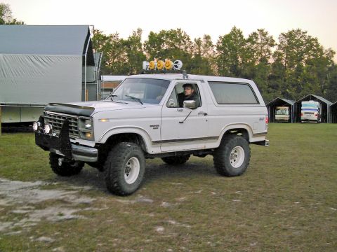 1986 Ford Bronco - A white Ford Bronco with off-road modifications is parked on a grassy field.