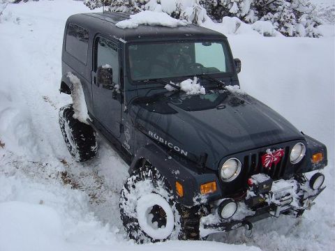 1986 Ford Bronco II - A dark green Jeep Wrangler Rubicon navigates through deep snow, equipped with a winch for challenging terrain.