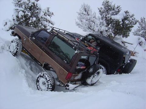 1986 Ford Bronco II - Two SUVs are stuck in the snow, with trees also covered in snow.