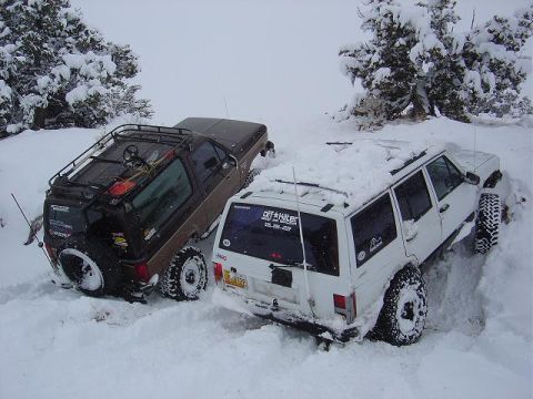 1986 Ford Bronco II - Two off-road vehicles are partially buried in snow, with only their tops and tires visible.