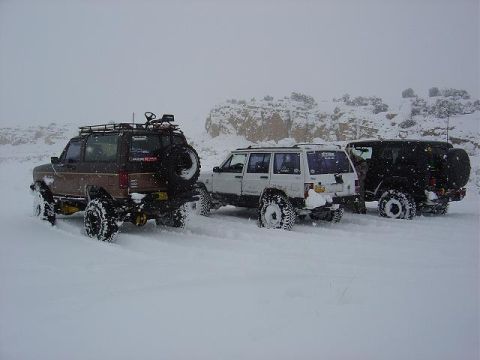 1986 Ford Bronco II - Three SUVs are stuck in the snow, with the lead vehicle being a brown Ford Bronco II.