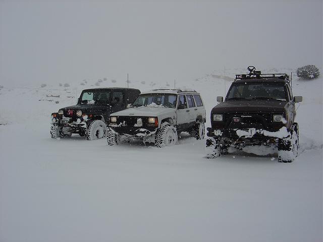 Three SUVs parked in deep snow, one black Jeep Wrangler, one white Jeep Cherokee, and one dark SUV