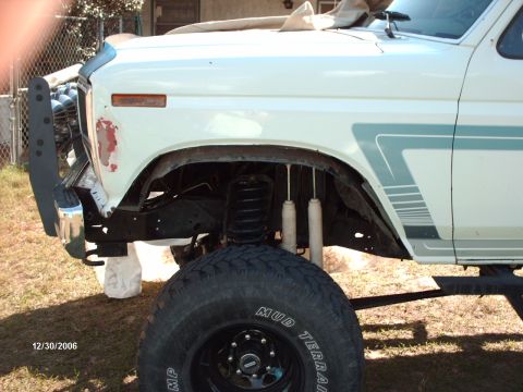 1982 Ford F-100 - White older Ford pickup with teal lower body stripes, viewed from the front-left with the driver's fender area exposed showing coil springs…