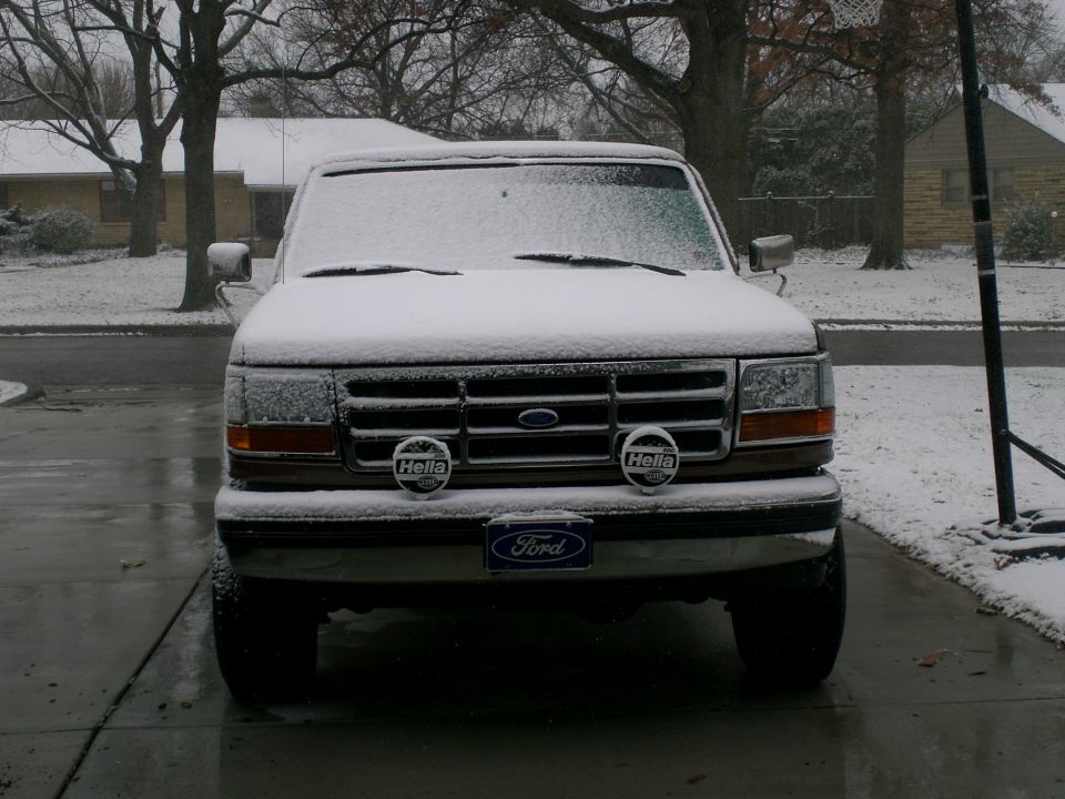 Snow-dusted Ford truck front end with brush guard in driveway