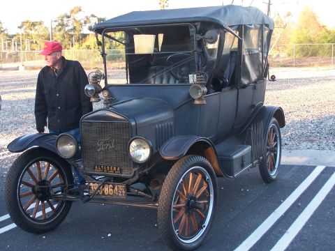 1990 Ford Bronco - A man stands next to a vintage Ford Model T touring car parked on asphalt with painted lines.
