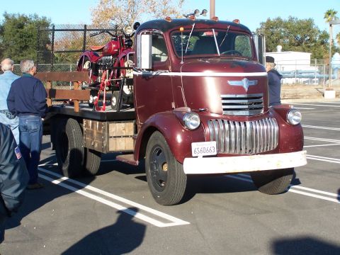 1990 Ford Bronco - A maroon flatbed truck transports a red motorcycle, viewed from the front.