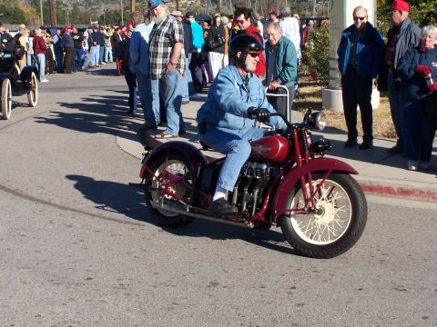 1990 Ford Bronco - A rider on a classic red motorcycle passes by onlookers at an event.