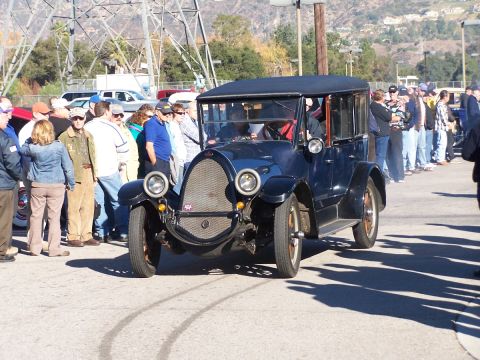 1990 Ford Bronco - A vintage dark blue sedan is on display, drawing a crowd of onlookers.