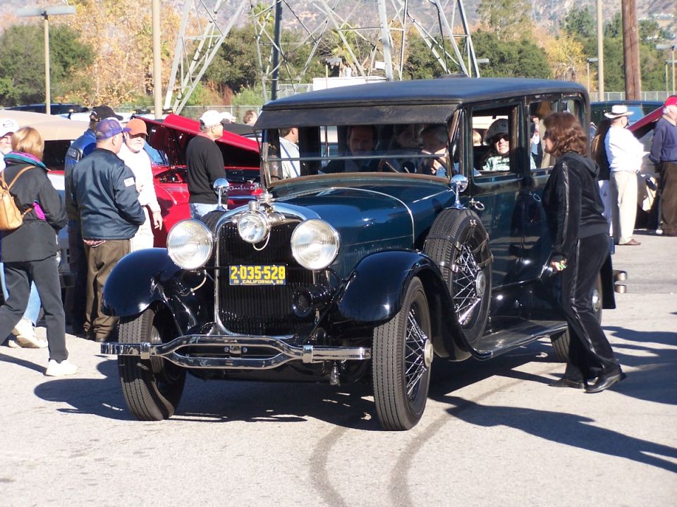 Vintage dark green sedan with a spare tire on the side, license plate 2-035-528. Other cars and people are visible in the background