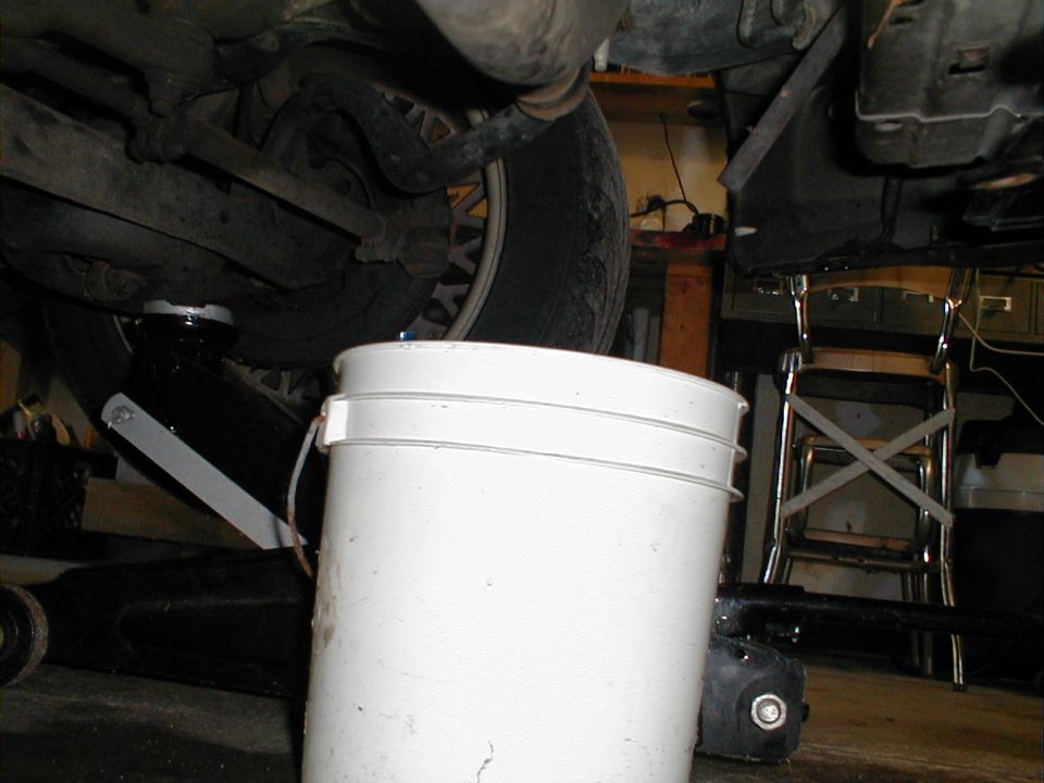 Undercarriage of a vehicle with a white bucket collecting fluid, tire visible