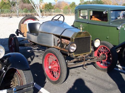 1990 Ford Bronco - A custom hot rod, possibly a modified Ford Model T, is parked next to a green sedan.