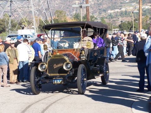 1990 Ford Bronco - A black Overland touring car from an earlier era is on display, with onlookers gathered around.