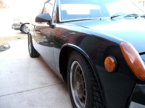 1974 Porsche 914 - A black sports car is parked on a concrete driveway, with another vehicle visible in the background.