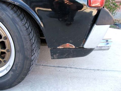 1974 Porsche 914 - Close-up of a black car's rear quarter panel showing rust damage and chrome exhaust pipes.