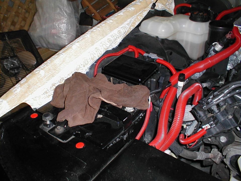 Engine bay with red wiring, battery, and a brown cloth. Supermotors.net logo visible