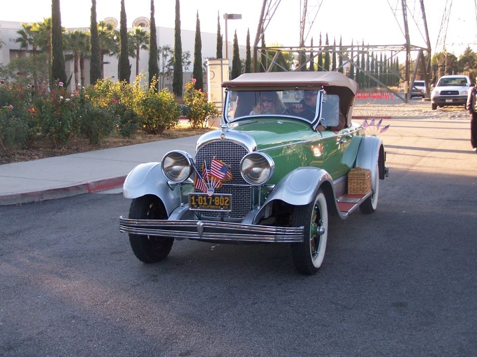 Green convertible with silver fenders and a tan top, driving on a street. License plate reads 1-017-802