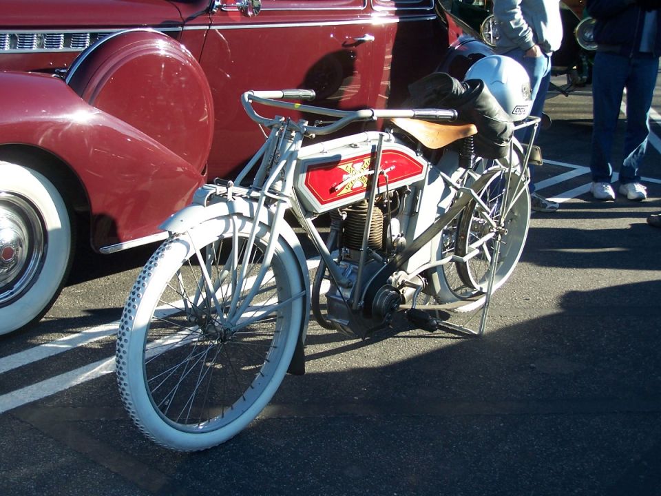Antique motorcycle with white tires parked next to a red classic car