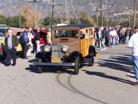 1990 Ford Bronco - A vintage woodie station wagon is parked in a lot with other cars and people milling around.