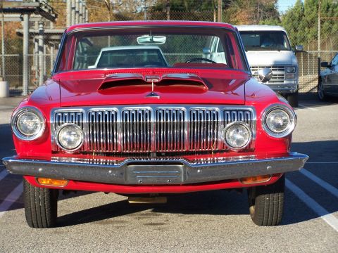 1990 Ford Bronco - A red classic car with a prominent chrome grille and dual headlights is parked in a lot.