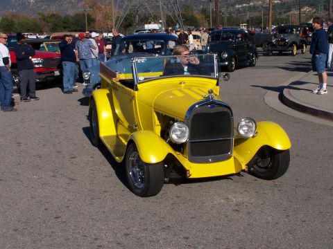 1990 Ford Bronco - A yellow hot rod roadster is parked on a street with other vehicles and people around.
