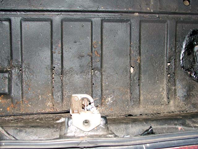 Rusty ribbed black metal panel with beige latch and wiring at bottom