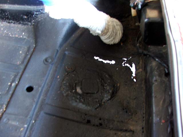 Black painted vehicle floor pan with stamped recess, drain holes, and cloth swab overhead