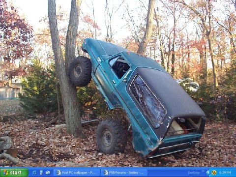 1989 Ford Bronco - This off-road vehicle appears to be stuck in a precarious position between two trees.