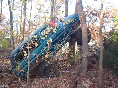 1989 Ford Bronco - A green SUV is stuck between trees after an apparent crash in a wooded area.