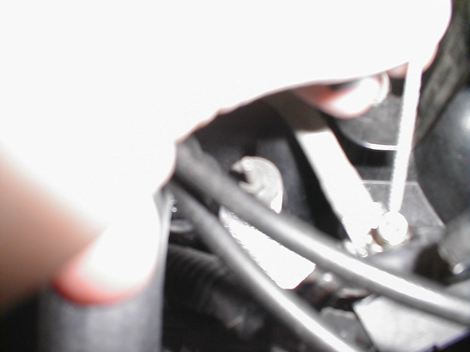 Close-up of engine bay with a hand holding a tool near hoses and wires
