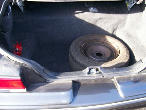 2001 Ford Crown Victoria - The trunk of a vehicle, showing the spare tire and a red emergency tool, with dark grey carpeting.
