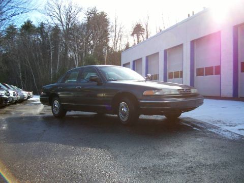 2001 Ford Crown Victoria - A dark 2001 Ford Crown Victoria is parked outside a building with multiple garage doors.