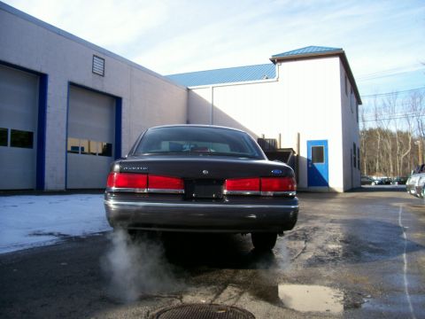 2001 Ford Crown Victoria - A dark sedan emits smoke from its exhaust pipe while parked in front of a commercial building.