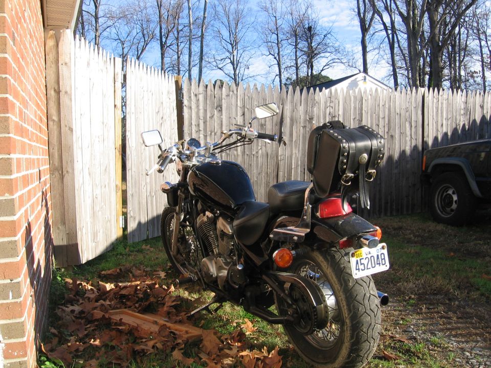 Black V-twin cruiser motorcycle with studded leather trunk parked by a wood fence