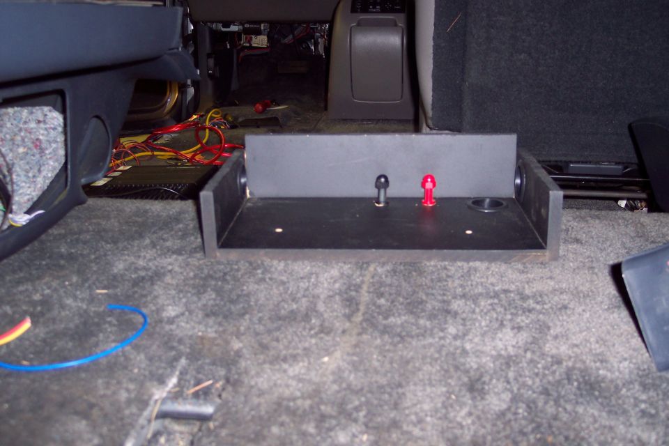 Custom subwoofer box with red and black terminal posts and wiring visible on vehicle carpet