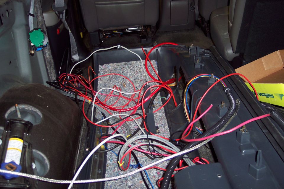 Vehicle interior with seats removed, showing a mess of red, white, and grey wires and insulation