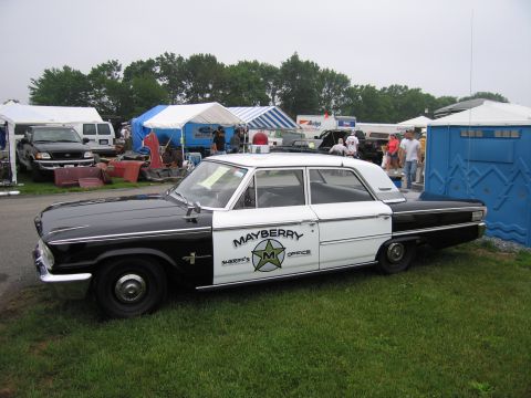 1991 Ford LTD Crown Victoria - Side view of a black-and-white vintage sedan marked Mayberry Sheriff's Office with a star door emblem, parked on grass at an outdoor event.