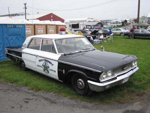 1991 Ford LTD Crown Victoria - Front three-quarter view of a black-and-white Ford sedan marked Mayberry Sheriff's Office with star emblem and roof beacon, at a grassy sho…