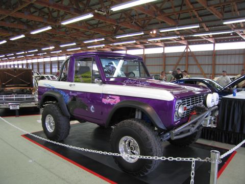 1991 Ford LTD Crown Victoria - Front three-quarter view of a purple-and-white lifted early Ford Bronco with big tires and Bronco fender script, on a display platform indo…