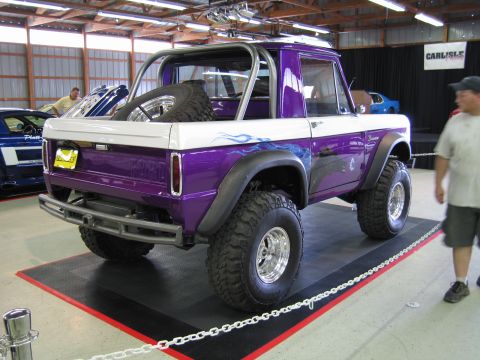 1991 Ford LTD Crown Victoria - Rear three-quarter view of a lifted purple-and-white early Ford Bronco with roll bar, spare tire and oversized tires, on an indoor show dis…