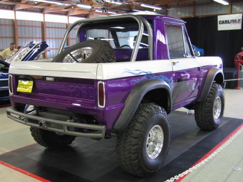 1991 Ford LTD Crown Victoria - Rear quarter view of a lifted purple-and-white early Ford Bronco with FORD tailgate lettering, roll bar and big tires, on an indoor display…