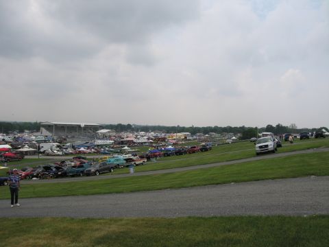 1991 Ford LTD Crown Victoria - broad view over a busy outdoor car-show field with rows of parked vehicles, tents and grandstands under heavy gray clouds.