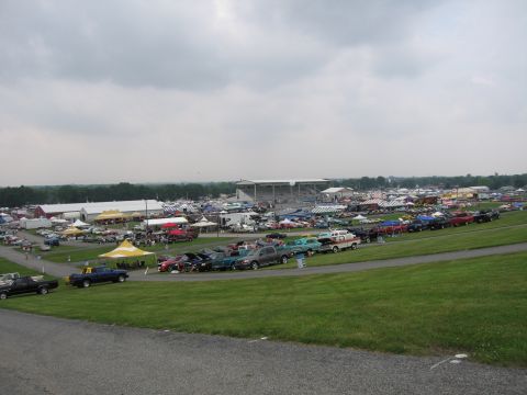 1991 Ford LTD Crown Victoria - Rows of cars, pickups and vendor tents cover a large grassy show field with grandstands in the distance under an overcast sky.
