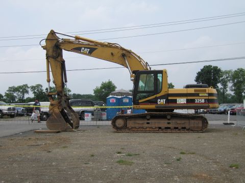 1991 Ford LTD Crown Victoria - yellow Caterpillar 325B tracked hydraulic excavator with its boom and bucket sits on a dirt lot near caution tape and parked vehicles.