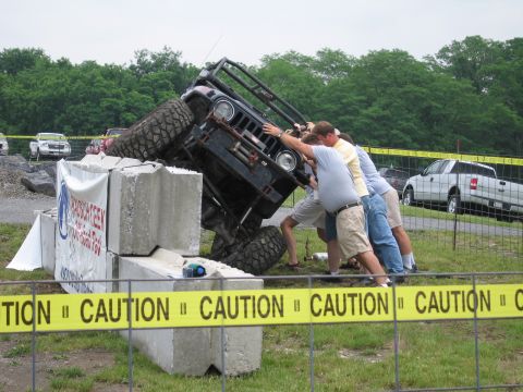 1991 Ford LTD Crown Victoria - group of men push a black tube-frame off-road vehicle perched on stacked concrete blocks, with a parked pickup and SUVs in the background.