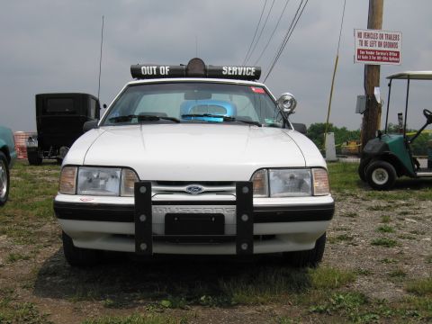 1991 Ford LTD Crown Victoria - Front view of a white fox-body Ford Mustang police car with a brush/push bar, roof light bar, and an Out of Service banner across the winds…