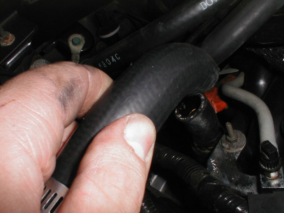 Hand holding a black hose in an engine bay, with visible hoses and connectors