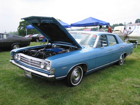 1991 Ford LTD Crown Victoria - Front three-quarter view of a light blue 1960s Ford four-door sedan with open hood and stacked dual headlights at an outdoor car show.